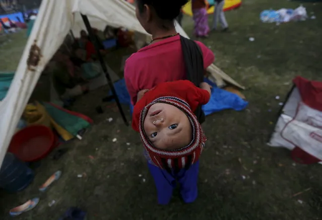 An earthquake victim carries her baby on her back as she stands outside her makeshift shelter on open ground in the early hours in Kathmandu, Nepal April 28, 2015. (Photo by Adnan Abidi/Reuters)
