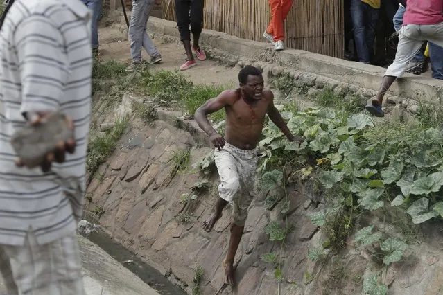 Jean Claude Niyonzima, a suspected member of the ruling party's Imbonerakure youth militia, flees from his house into a sewer under a hail of stones thrown by a mob protesting against President Pierre Nkurunziza's decision to seek a third term in office, in the Cibitoke district of Bujumbura, Burundi, Thursday May 7, 2015. (Photo by Jerome Delay/AP Photo)