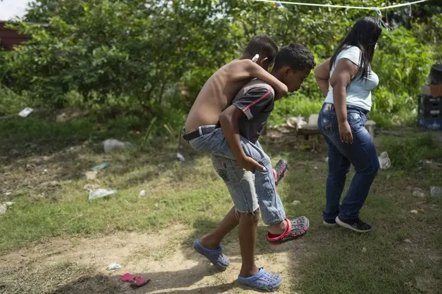 Angel Cespedes is carried by his brother Eliecer to their home after both Angel and their mother, Yohelys Cespede, return from receiving their dialysis treatments, in Valles del Tuy on the outskirts of Caracas, Venezuela, Monday, November 8, 2021. Angel has relied on dialysis since he was diagnosed with chronic kidney disease in 2017. Except for a few charity-aided cases, poor Venezuelan children have not received organ or bone marrow transplants since 2017. (Photo by Ariana Cubillos/AP Photo)