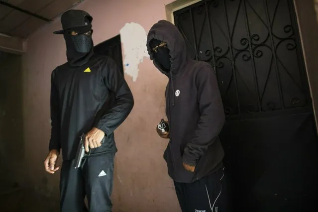 Masked criminals who go by the name “El Negrito”, right, and “Dog”, and are members of the Crazy Boys gang, hold their guns at their safe-house in the Petare slum of Caracas, Venezuela, Monday, May 13, 2019. Dog said he has no trouble finding ammunition for his guns on the black market, but that the challenge is paying for them in a country where the average person earns $6.50 a month. “A pistol used to cost one of these bills”, he said, crumbling up a 10 bolivar bill that can no longer be used to buy a single cigarette. “Now, this is nothing”. (Photo by Rodrigo Abd/AP Photo)