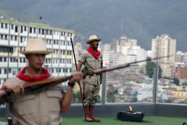 A soldier (R) sings as he holds a stick with fire to shoot a cannon at 4:25 p.m., the time the death of Venezuela's late president Hugo Chavez was announced, at the 4F military fort in Caracas, June 30, 2015. (Photo by Jorge Dan Lopez/Reuters)