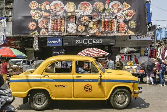 A yellow ambassador taxi passes by a bill board of variety of foods of an upcoming restaurant branch in Kolkata, India, 17 April, 2022. (Photo by Indranil Aditya/NurPhoto via Getty Images)