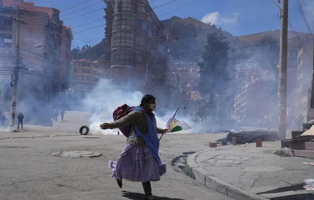 An anti-government coca farmer runs away from tear gas fired by riot police near the coca market in La Paz, Bolivia, Thursday, September 23, 2021. The anti-government coca farmers tried to take over the coca market by force, after losing control when another group of coca growers elected a new leader. (Photo by Juan Karita/AP Photo)