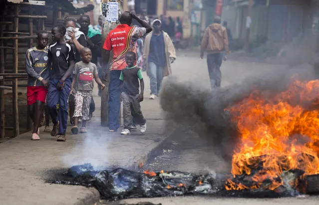 Young boys walk past a barricade of burning tyres, erected by demonstrators calling for the disbandment of the national electoral commission over allegations of bias and corruption, in the Kibera slum of Nairobi, Kenya Monday, June 6, 2016. While demonstrations led by opposition leaders in the capital were largely peaceful, police in the western town of Kisumu tear-gassed demonstrators who responded by throwing stones and witnesses say some people were killed by police. (Photo by Ben Curtis/AP Photo)