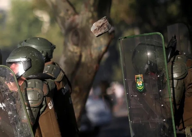 A rock flies past members of security forces standing behind riot shields during a protest against Chile's government in Santiago, Chile on December 18, 2019. (Photo by Ricardo Moraes/Reuters)