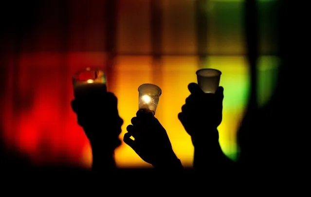 People hold up candles against a rainbow lit backdrop during a vigil for those killed in a mass shooting at the Pulse nightclub downtown Monday, June 13, 2016, in Orlando, Fla. A gunman has killed dozens of people in a massacre at a crowded gay nightclub in Orlando on Sunday, making it the deadliest mass shooting in modern U.S. history. (Photo by David Goldman/AP Photo)