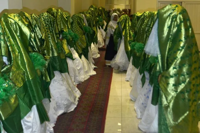 Brides stand inside a wedding hall as they wait for the start of a mass marriage ceremony in Kabul on June 13, 2022. Dozens of Afghan women concealed in thick green shawls were married off in an austere mass wedding in Kabul, in a ceremony attended by hundreds of guests and gun-toting Taliban fighters. (Photo by Sahel Arman/AFP Photo)