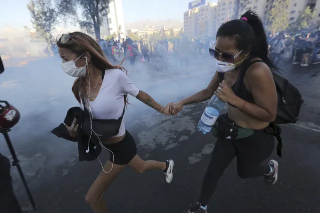 In this December 20, 2019, file photo, anti-government demonstrators run from a cloud of teargas during clashes with police in Santiago, Chile. Last year, face masks were an act of rebellion, a signature piece of clothing associated with protesters in  who wore them to protect against tear gas or to conceal their identities from authorities. These same masks are now ubiquitous around the world – worn by people from China and Iran, to Italy and America, seeking to protect against the coronavirus. The vast majority of people recover from the new virus. (Photo by Fernando Llano/AP Photo)