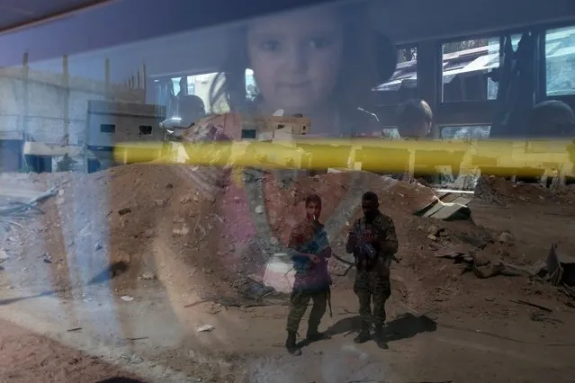 Syrian government troops are seen reflected on the window of a bus carrying people as part of an evacuation from the town of Daraya outside the capital Damascus on August 26, 2016, under a deal agreed between the government and opposition fighters after a four-year army siege. State news agency SANA, which announced the deal on Thursday, said 700 rebels and their families would go to rebel-controlled Idlib and thousands of civilians would be taken to government reception centres. (Photo by Youssef Karwashan/AFP Photo)