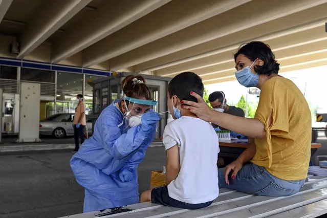 A health worker wearing protective gear takes swab samples from tourists to test for the coronavirus, at Promahonas border crossing with Bulgaria, which is the only land border into Greece that is open on Monday, July 6, 2020. Dozens of vehicles of Serb holidaymakers who were trapped at the Greek border overnight have been allowed to cross into Greece after a ban on the entry of people from Serbia came into effect due to a coronavirus flare-up in Serbia. (Photo by Giannis Papanikos/AP Photo)