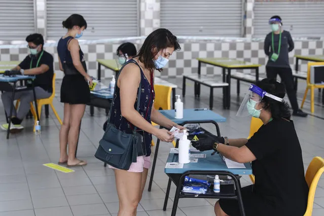 Voters, wearing face masks, verify their identities with polling officers at the Chung Cheng High School polling center before casting their votes in Singapore, Friday, July 10, 2020. Singaporeans began voting in a general election that is expected to return Prime Minister Lee Hsien Loong's long-governing party to power. (Photo by AP Photo/Stringer)