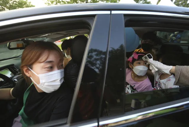 A young girl has her temperature checked as she arrives to watch a drive-in concert at the Gyeongbok Palace parking lot in Seoul, South Korea, Friday, July 17, 2020. The concert's aim is to provide entertainment for people during the coronavirus outbreak. (Photo by Ahn Young-joon/AP Photo)