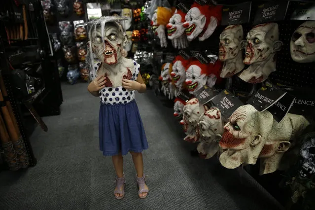 In this September 2, 2015 photo, six-year-old Olivia Vlaicu, of Maywood, N.J., tries on an “ancient zombie” mask at the Spirit Halloween store, in Paramus, N.J. Spirit Halloween, a chain of more than 1,150 pop-up shops across the country, has reincarnated a former Staples store and filled it with 4,000 costumes and accessories with themes ranging from zombies to superheroes and princesses to prison inmates. (Photo by Mel Evans/AP Photo)