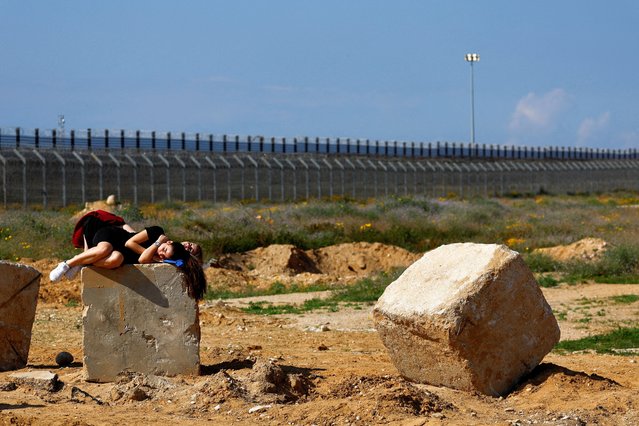 Demonstrators rest during a protest against the delivery of humanitarian aid to Gaza and demand the immediate release of Israeli hostages kidnapped in the deadly October 7 attack, as trucks waiting to enter Gaza from Egypt are seen in the background, amid the ongoing conflict between Israel and the Palestinian Islamist group Hamas, at the Kerem Shalom Crossing, Israel, on February 20, 2024. (Photo by Susana Vera/Reuters)