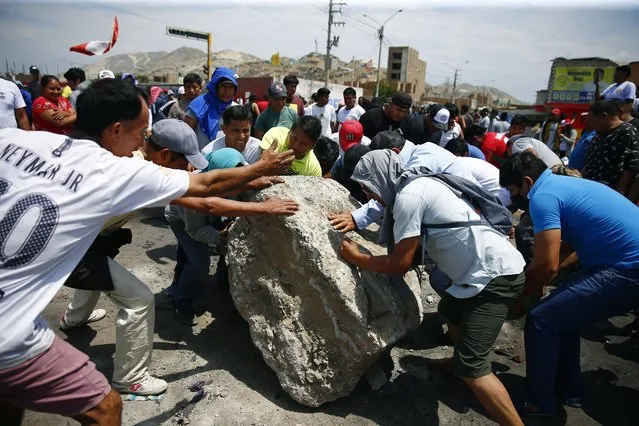 Supporters of ousted Peruvian President Pedro Castillo work together to roll a boulder onto the Pan-American North Highway during a protest against his detention, in Chao, Peru, Thursday, December 15, 2022. (Photo by Hugo Curotto/AP Photo)