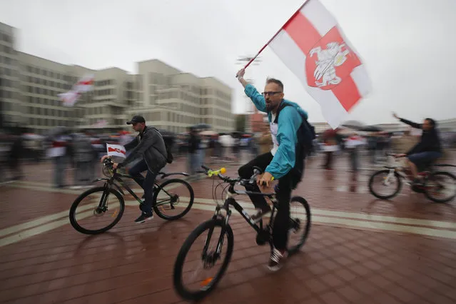 Belarusian opposition supporters ride bicycles and wave an old Belarusian national flags during a protest rally in front of the government building at Independent Square in Minsk, Belarus, Wednesday, August 19, 2020. The authoritarian leader of Belarus complained that encouragement from abroad has fueled daily protests demanding his resignation as European Union leaders held an emergency summit Wednesday on the country's contested presidential election and fierce crackdown on demonstrators. (Photo by Dmitri Lovetsky/AP Photo)