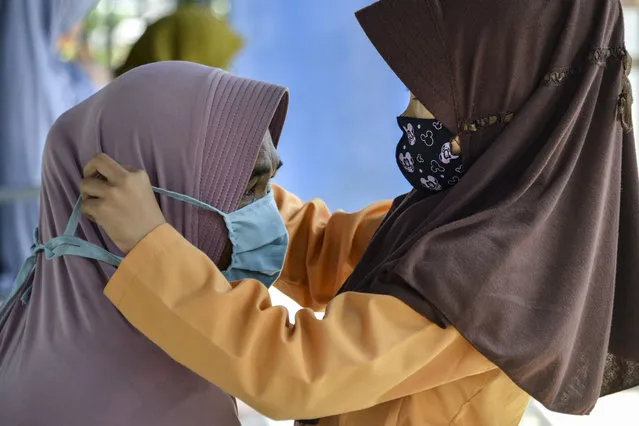 A child adjusts her mother's face mask as a preventive measure to curb the spread of the COVID-19 coronavirus while waiting for a bus in Banda Aceh on August 22, 2020. (Photo by Chaideer Mahyuddin/AFP Photo)