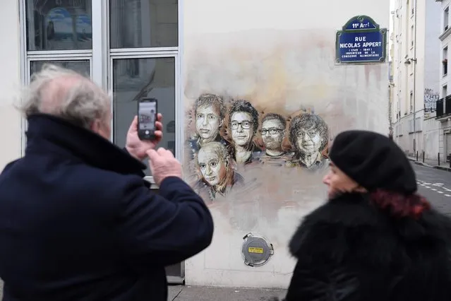 A man takes a picture of portraits (LtoR) of late French satirical weekly Charlie Hebdo's deputy chief editor Bernard Maris, French cartoonists Georges Wolinski, Bernard Verlhac (aka Tignous), Charlie Hebdo editor Stephane Charbonnier (aka Charb) and Jean Cabut (aka Cabu) near the magazine's offices at Rue Nicolas Appert, in Paris on January 7, 2018, on the third anniversary of the jihadist attack on French satirical magazine Charlie Hebdo. Two French jihadists who had sworn allegiance to al-Qaeda killed 11 people at Charlie Hebdo's offices in 2015 over the staunchly atheist magazine's satirical coverage of Islam and the prophet Mohammed. (Photo by Christophe Archambault/AFP Photo)