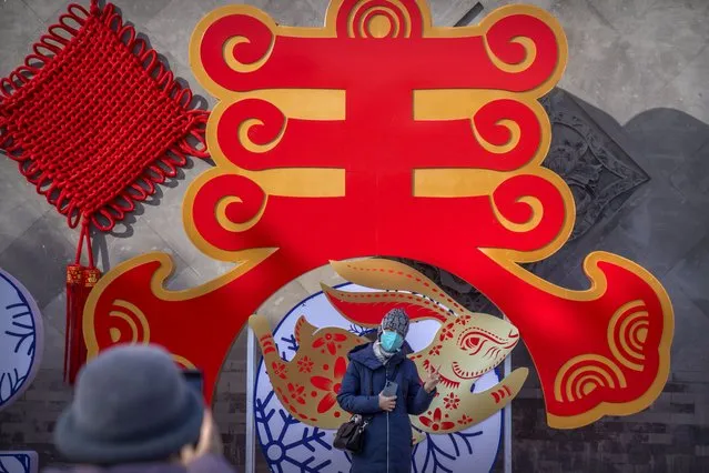 A visitor wearing a face mask poses for a photo in front of a New Year-themed display at a public park in Beijing on the first day of the Lunar New Year holiday, Sunday, January 22, 2023. (Photo by Mark Schiefelbein/AP Photo)