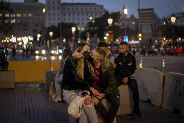 A couple wearing masks kiss in downtown Barcelona, Spain, Thursday, October 29, 2020. Spain's Parliament on Wednesday endorsed an extension of the state of emergency declared by the government until May 9. The measure puts into place a nightly curfew and allows regions to impose more restrictions like the ones the Catalonia announced, limiting movement outside city limits on weekends. (Photo by Emilio Morenatti/AP Photo)