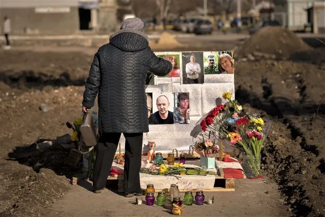A woman touches photos of victims on a makeshift memorial for those killed when an apartment block was hit by an airstrike, one year ago, in Borodyanka, Ukraine, Thursday, March 2, 2023. (Photo by Vadim Ghirda/AP Photo)
