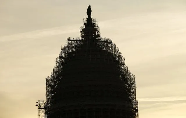 A worker (L) reaches for supplies while working atop the scaffolded dome of the U.S. Capitol in Washington December 4,  2014. The Capitol Dome is undergoing a multi-year restoration to stop the current level of deterioration in the Dome's cast iron as well as ensuring the protection of the interior of the Dome and Rotunda. The restoration project includes removal of old paint, repairs to the cast iron and stone, and repainting. (Photo by Kevin Lamarque/Reuters)