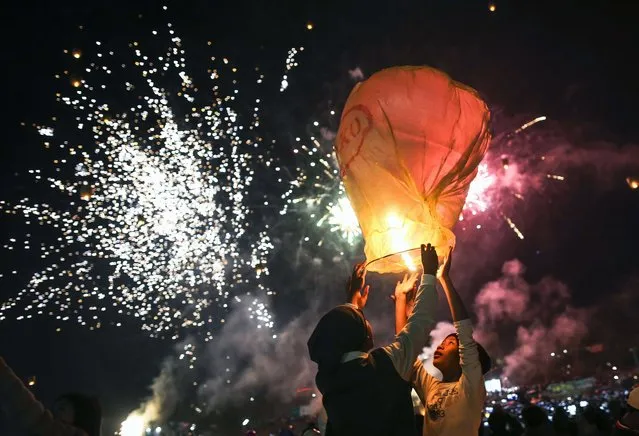 This picture taken on November 18, 2015 shows young participants preparing to release a hot-air balloon during the Tazaungdaing Lighting Festival at Taunggyi in Myanmar's northeastern Shan State. Every year in November as the full moon approaches, tens of thousands of people from all over the country gather in Taunggyi for the colourful hot-air balloons festival during which balloons lift fireworks or lanterns which illuminate the sky at night while balloons of all shapes are flown during the day. (Photo by Ye Aung Thu/AFP Photo)