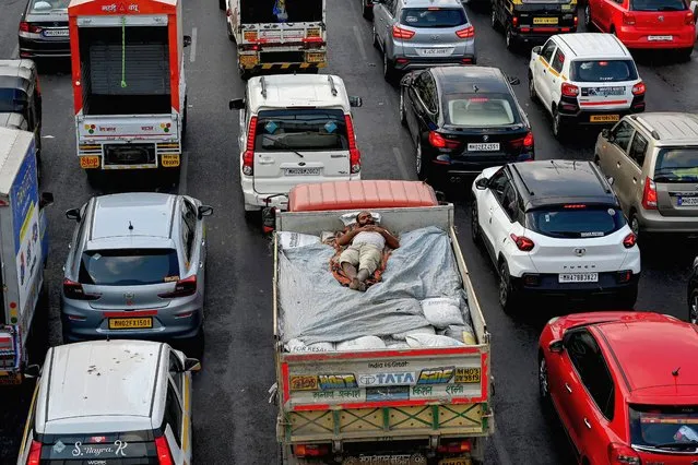 A labourer sleeps on the back of a delivery truck as vehicles are stuck in bumper to bumper traffic on the Western Express Highway in Mumbai on April 25, 2023. (Photo by Indranil Mukherjee/AFP Photo)
