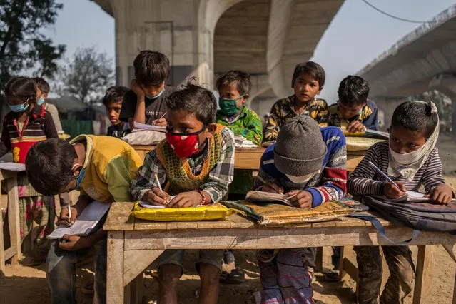 Underprivileged children sit at desks underneath a flyover at an improvised classroom set up at a construction site on December 09, 2020 in New Delhi, India. Many underprivileged children are unable to afford the laptops or tablet computers needed for online classes, leaving them without access to education as the Covid-19 pandemic rages across India. The improvised school, set up by graduate students who are still looking for work, is located at a construction site underneath a metro railway track in the dusty streets of the country's capital. The pandemic is hit the underprivileged members of society the hardest, forcing millions of people out of work, out of homes, and back into destitution, as the country quickly approaches a tally of 10 million infections. (Photo by Anindito Mukherjee/Getty Images)