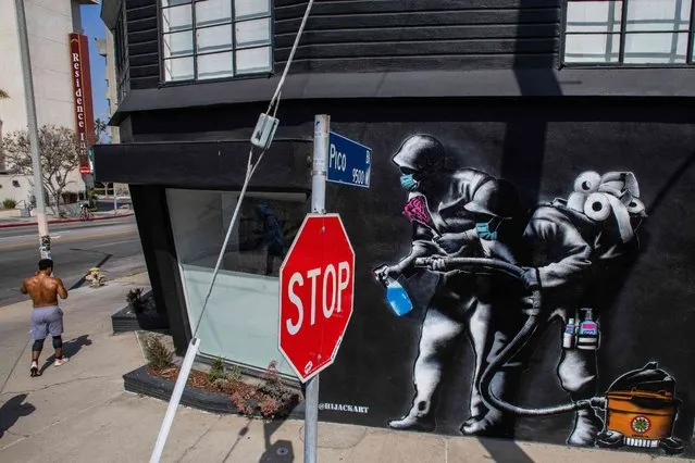 A man walks by a mural by Hijackhart, where soldiers wearing face masks fight COVID-19 with disinfectant and hand sanitizers during the coronavirus pandemic on April 4, 2020 in Los Angeles. (Photo by Apu Gomes/AFP Photo)