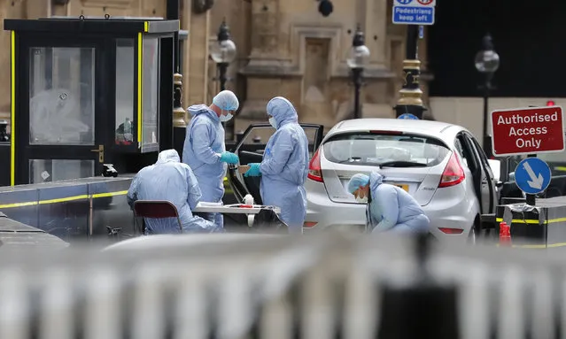 Forensics officers work on the car that crashed into security barriers outside the Houses of Parliament to the right of a bus in London, Tuesday, August 14, 2018. Authorities said in a statement Tuesday that a man in his 20s was arrested on suspicion of terrorist offenses after a silver Ford Fiesta collided with a number of cyclists and pedestrians before crashing into the barriers during the morning rush hour. (Photo by Frank Augstein/AP Photo)