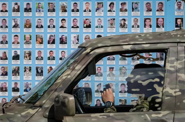 A Ukrainian serviceman smokes in a military car next to the memory wall of fallen defenders of the country after a funeral ceremony his brothers-in-arms, who were recently killed in fights against Russian troops, amid Russia's attack on Ukraine, in central Kyiv, Ukraine on August 22, 2023. (Photo by Gleb Garanich/Reuters)