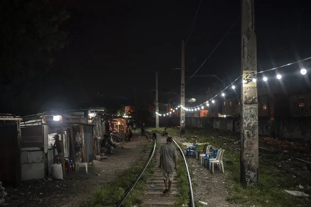 A man walks on the train tracks as people gather in an area known as “cracolandia” or crackland, amid the COVID-19 pandemic in Rio de Janeiro, Brazil, Friday, March 19, 2021. “Cracolandias” are open-air bazaars found in some Rio de Janeiro slums where crack cocaine users can buy rocks of the drug and smoke it in plain sight, day or night. (Photo by Felipe Dana/AP Photo)