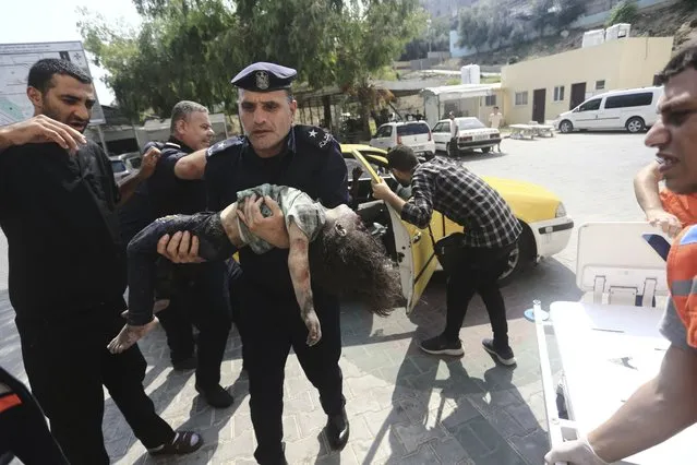 A Hamas police officer carries a wounded girl into a hospital in Beit Lahiya, Gaza Strip, Sunday, October 8, 2023. (Photo by Mahmoud Essa/AP Photo)