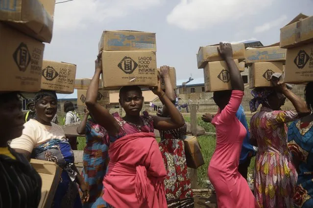 Residents of Oworonshoki Slum carry their food parcels distributed by the Lagos Food Bank Initiative, a non-profit nutrition focused initiative committed to fighting hunger and solving problems of Malnutrition for poor communities, in Lagos, Nigeria, Saturday, July 10, 2021. (Photo by Sunday Alamba/AP Photo)