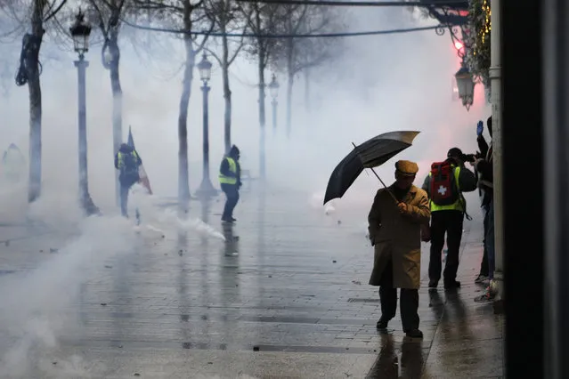 A man makes his way through tear gas as demonstrators protest on the Champs-Elysees avenue, Saturday, December 15, 2018 in Paris. (Photo by Kamil Zihnioglu/AP Photo)