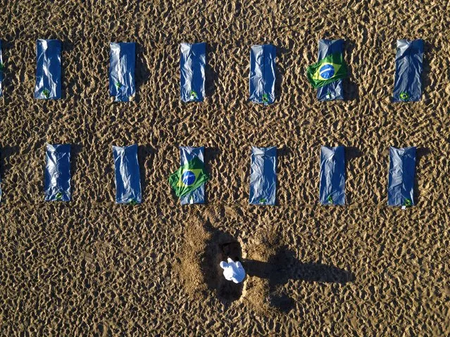 An activist from the NGO “Rio de Paz” digs a mock grave in the sand by symbolic body bags on Copacabana beach to protest the government's handling of the COVID-19 pandemic and to mark the milestone of 400,000 virus deaths in Rio de Janeiro, Brazil, Friday, April 30, 2021. (Photo by Lucas Dumphreys/AP Photo)