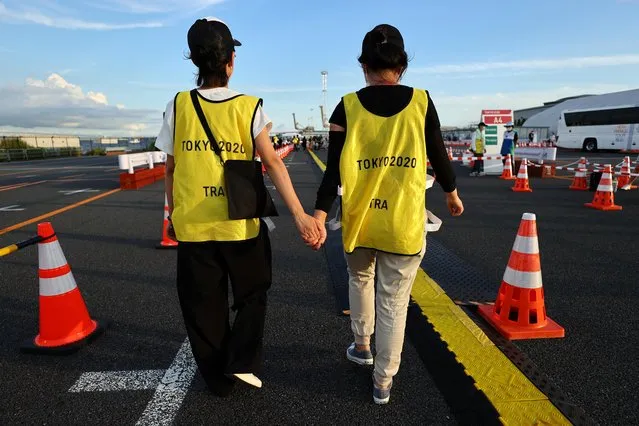 Volunteers walk holding their hands at a transport station during the Tokyo 2020 Olympic Games in Tokyo, Japan July 23, 2021. (Photo by Jorge Silva/Reuters)