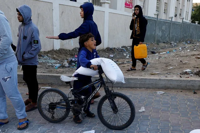 A Palestinian child carries flour bags distributed by UNRWA in Rafah, in the southern Gaza Strip on November 21, 2023. (Photo by Ibraheem Abu Mustafa/Reuters)