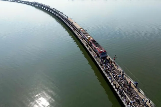 This aerial photograph taken on November 4, 2023 shows tourists travelling aboard the popular “Floating train” taking photographs along the railway tracks during a stop in the middle of Pasak Jolasid Dam, Thailand's biggest reservoir in Lopburi province. A lone boatman watched the spectacle of Thailand's so-called “floating train” as selfie-seeking passengers soaked up the water views after disembarking from carriages stopped on a narrow bridge. (Photo by Manan Vatsyayana/AFP) 