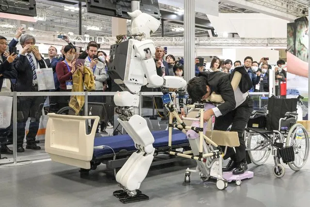 A robot (L) helps move a man into a wheelchair, during a demonstration at the Kawasaki booth on the first day of the 2023 International Robot Exhibition at the Tokyo International Exhibition Center in Tokyo on November 29, 2023. (Photo by Richard A. Brooks/AFP Photo)