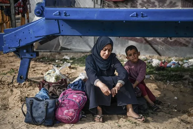 A Palestinian woman sits on a stone with a baby as Palestinian families, seeking refuge from Israeli attacks on Gaza, establish makeshift tents in vacant areas to ensure their safety in Rafah, Gaza on December 27, 2023. Palestinians who have financial insufficiency, continue their lives by waiting for aid from non-governmental organizations. (Photo by Abed Zagout/Anadolu via Getty Images)