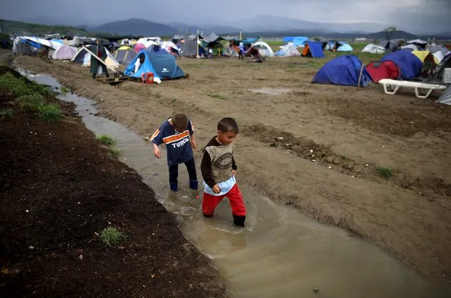 Boys walk through water at a makeshift camp for migrants and refugees at the Greek-Macedonian border near the village of Idomeni, Greece, April 9, 2016. (Photo by Stoyan Nenov/Reuters)