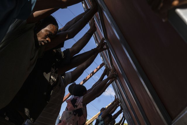 Neighbors raise a metal gate as they work to install it as a barricade against gangs, in the Petion-Ville neighborhood of Port-au-Prince, Haiti, Saturday, April 20, 2024. (Photo by Ramon Espinosa/AP Photo)