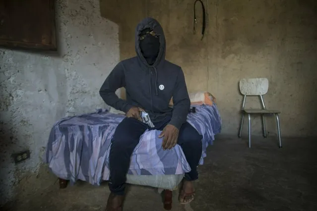 A masked gangster who goes by the nickname “El Negrito” poses for a portrait with his gun inside his gang's safe-house in the Petare slum of Caracas, Venezuela, Monday, May 13, 2019. The 24-year-old, who says he’s lost track of his murder count, is quick to gripe about how Venezuela’s failing economy is cutting into his profits and has considered leaving the trade in Venezuela and emigrating. (Photo by Rodrigo Abd/AP Photo)