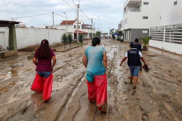 Women use bags to cover their feet and legs to walk on a street covered in mud following Cyclone Yaku in Punta Hermosa, Peru on March 15, 2023. (Photo by Sebastian Castaneda/Reuters)