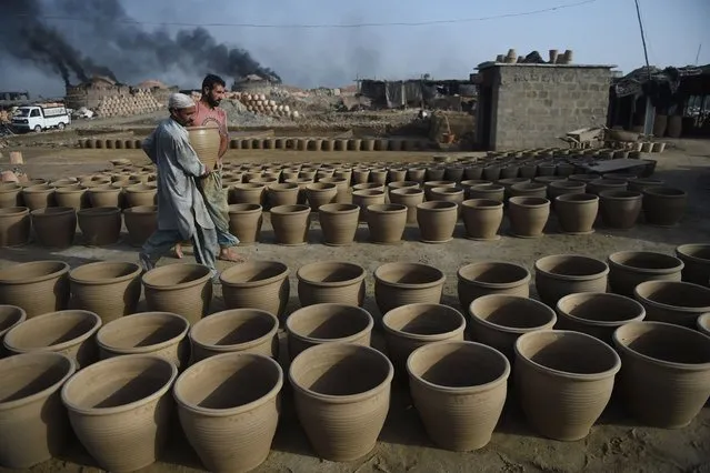 Potters place a clay pot to dry at a workshop in Karachi on February 23, 2022. (Photo by Rizwan Tabassum/AFP Photo)