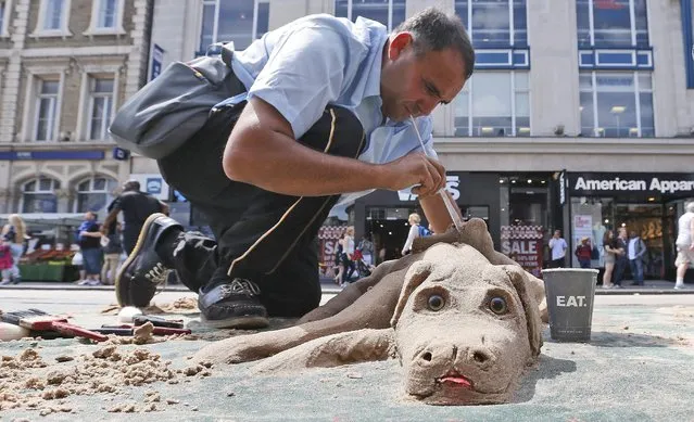Street artist Nikolas sculpts a sand puppy dog in London, Friday, July 17, 2015. To make money for living Nikolas takes beach sand to the streets of London and creates sculptures. (Photo by Frank Augstein/AP Photo)