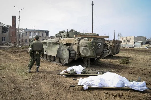Service members of pro-Russian troops stand next to bodies of personnel killed in fighting in the Ukraine-Russia conflict in the city of Mariupol, Ukraine on March 31, 2022. (Photo by Chingis Kondarov/Reuters)