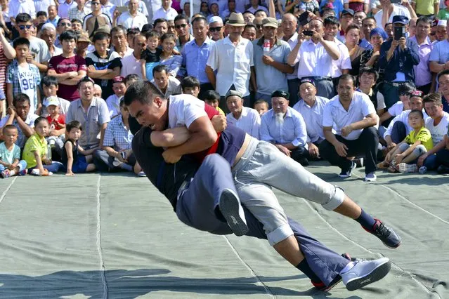People watch as contestants wrestle during ethnic minorities traditional games, to celebrate Eid al-Fitr, in Hami, Xinjiang Uighur Autonomous Region, China, July 19, 2015. (Photo by Reuters/China Daily)
